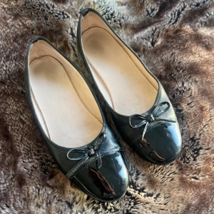 Ballerinaskor med rosett - Snygga svarta ballerinaskor i lack med en söt rosett på tån. Perfekta för en elegant touch.