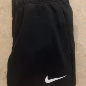 Svarta mjukis/tränings byxor från Nike - Snygga svarta mjukisbyxor från Nike med Dri-FIT-teknologi. Byxorna har en elastisk midja och en vit Nike-logga på benet. Perfekta för träning eller en avslappnad dag. Dessa byxor är helt perfekt och fungerar felfritt och är knappt använda. ABS! Pris går att diskuteras.