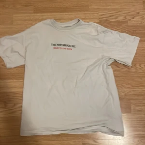 Vit t-shirt med The Notorious B.I.G. tryck - Säljer en vit t-shirt med tryck av The Notorious B.I.G. 'Ready to Die Tour'. Framsidan har text och baksidan ett ikoniskt bildtryck. Perfekt för fans av klassisk hiphop!
