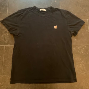 Svart t-shirt från Maison Kitsuné - Säljer en  svart t-shirt från Maison Kitsuné med en broderad räv på bröstet. Perfekt för en avslappnad look. T-shirten har korta ärmar i storlek large men passar medium