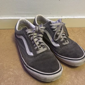 Gråa Vans skor storlek 41 - Säljer ett par grå sneakers från Vans med vit sula och klassisk snörning. Skorna har en ikonisk vit rand på sidan och är perfekta för en avslappnad stil. Storlek 41