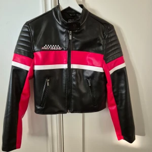 Skinnjacka - Jacka i skinnimitation i biker/racing stil från New Yorker. Jackan har en knapp upptill och dragkedjor i ärmarna. Den är mjuk i materialet. Endast använd vid ett tillfälle så den är i nyskick. Storlek S