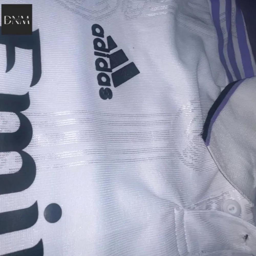 Säljer en vit Real Madrid fotbollströja från Adidas. Tröjan har korta ärmar och är i nyskick. Den har klubbens emblem på bröstet och sponsorloggan 'Emirates Fly Better' tryckt på framsidan. På baksidan står det 'VINI JR.' med nummer 20. . T-shirts.