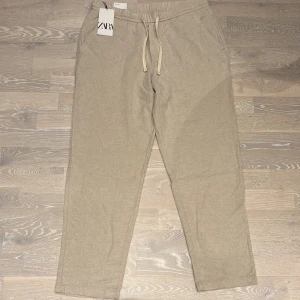 Beige linnebyxor från Zara - Säljer ett par snygga beige linnebyxor från Zara. De har en avslappnad passform med snörning i midjan för extra komfort. Perfekta för en somrig och avslappnad stil! Oanvända!