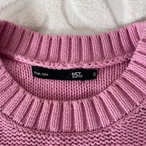 Rosa stickad tröja från 157 - Säljer en superfin rosa stickad tröja från lager 157. Den är gjord av 100% bomull. Tröjan har långa ärmar och en ribbad kant vid halsen, ärmsluten och nederkanten. Perfekt för att hålla sig varm och stilren under höst och vinter.