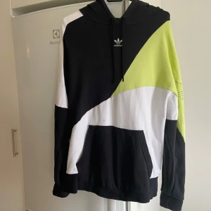 Flerfärgad hoodie från Adidas - Säljer en cool flerfärgad hoodie från Adidas i storlek 40/M. Tröjan är svart, vit och limegrön. Har en stor ficka fram och Adidas-loggan på ärmen. Tröjan är använd några gånger men har en fläck (enbart tvättad). Kanske går fixa med fläckborttagning. 