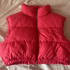 Rosa dunväst från NLY Trend - Säljer en superfin rosa dunväst från NLY Trend i storlek S. Västen har en dragkedja framtill och är perfekt för höst och vår. Den är både snygg och praktisk med en croppad passform som ger en modern look. Perfekt för att hålla värmen utan att komprom