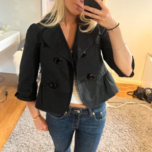 Jacka - Sjukt snygg och trendig svart trekvartsärmad jacka/kort kappa, mycket bra skick! Den har superfina ”rosetter” på ryggen och ärmarna som gör den unik. Perfekt nu till hösten💕 Köp via ”köp nu”💗