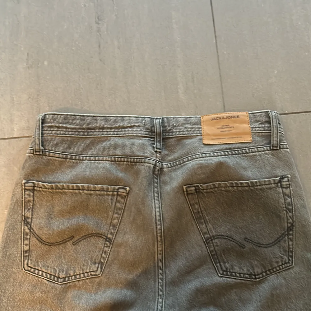 Säljer ett par grå jeans från Jack & Jones. De har en klassisk femficksdesign och en snygg, lite sliten look. Perfekta för en avslappnad stil. Passar både till vardags och fest!. Jeans & Byxor.