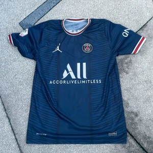 Blå PSG fotbollströja från Nike - Säljer en snygg blå PSG fotbollströja. Tröjan har korta ärmar och  det klassiska PSG-emblemet på bröstet.  Perfekt för alla fotbollsfans som vill visa sitt stöd för laget. Den är XL men passar M/L, köpt utomlands och ej från en officiell butik. 