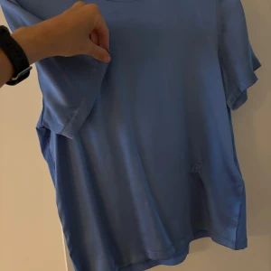 Blå t-shirt från Majestic - Säljer en snygg blå t-shirt från Majestic i storlek M. Den har en enkel och stilren design med korta ärmar och en liten broderad logga längst ner. Perfekt för vardagsbruk eller en avslappnad dag ute. Materialet känns mjukt och skönt mot huden.