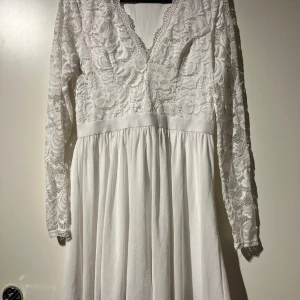 Vit spetsklänning med lång ärm - Säljer en superfin vit klänning med v-ringad spetsdetaljer på överdelen och långa ärmar. Kjolen är flödande och ger en elegant look. Perfekt för sommarens fester eller kanske till ett bröllop? 🎆