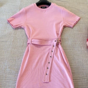 Rosa ribbad klänning med bälte - Säljer en superfin rosa ribbad klänning med korta ärmar och ett matchande bälte i midjan. Klänningen har en söt volangdetalj vid ärmslut och nederkant. Perfekt för sommarens alla fester! 💖