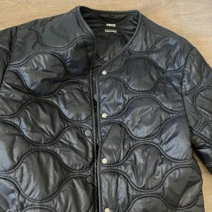 Svart quiltad jacka från MNG - Säljer en snygg svart quiltad jacka från mango. Den har en cool vågig quiltad design och knäpps med knappar framtill. Perfekt för höst och vår när du vill ha något stilrent och bekvämt. Jackan är långärmad och har en normal passform, knappt använd.