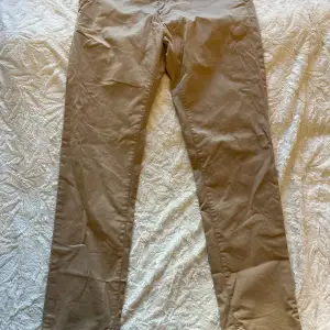 Säljer ett par snygga beige chinos från Gant. De är i storlek 176 cm, vilket motsvarar ungefär 16 år. Byxorna har en klassisk design med knappar och är perfekta för både vardag och lite mer uppklädda tillfällen. Materialet känns skönt och hållbart.