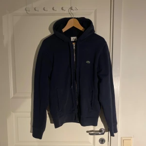 Lacoste hoodie - Säljer en marinblå Lacoste hoodie uppskattad storlek S. Plagget är i bra skick utan defekter. Mycket bra helhetsintryck! Passar dig ca 175-180
