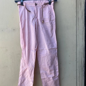 Rosa byxor med snörning - Säljer ett par ljusrosa byxor i storlek M. De har en avslappnad passform med snörning i midjan och knappar framtill. Perfekta för en casual look eller en dag på stan!