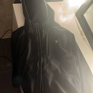 Svart Lyle scott jacka  - Säljer nu min Lyle scott jacka då jag vuxit ur den. Väldigt bra jacka, bra passform, relativt vattentät, lagom varm att ha under hösten, 2 öppna fickor plus en stängbar vid bröstet. Vindtät perfekt när de blåser o duggregnar lite. Bästa luvan!