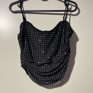 Svart glittrig korsettopp - Säljer en snygg svart korsettopp med glittriga detaljer. Toppen har smala axelband och en åtsittande passform som ger en elegant look. Perfekt för festliga tillfällen!