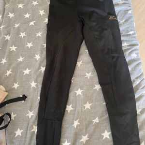 Svarta ridleggings i storlek XS - Säljer ett par svarta ridleggings i storlek XS. De är högmidjade och har en snygg design med detaljer på sidorna. Perfekta för ridning och ger en bekväm passform. Inte mycket använda så i bra skick! Är ett pyttelitet hål vid vaden men det syns knappt