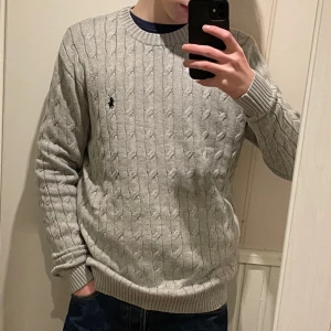 Grå stickad Kofta från Polo Ralph Lauren - Säljer en stilren grå kabelstickad tröja från Polo Ralph Lauren med den klassiska loggan på bröstet. Tröjan har rund hals och långa ärmar med ribbade muddar. Perfekt för en avslappnad och snygg look. Lite större i storleken, han på bilden är 175cm. 💰 (Pris går att diskuteras vid snabb affär)💰 INGA RETURER!🚨