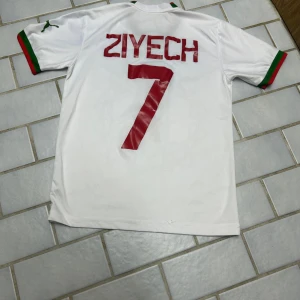 Marockansk landslagströja / Hakim Ziyech tröja (VM 2022) - Ännu en legendarisk fotbollströja från VM 2022 då Hakim Ziyech ledde Marocko till semifinal. En väldigt fin tröja med exemplariskt skick och oanvänd.