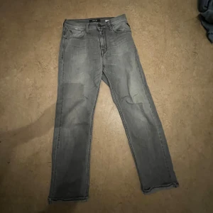 Grå jeans från Replay - Snygga grå jeans från Replay med klassisk femficksdesign. De har en rak passform och är perfekta för en avslappnad stil. Jeansen har en dragkedja och knapp framtill. Fast den har ett litet hål vid byxfickan. Vikningen vid fötterna sitter fast. 150cm