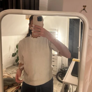 Vit stickad tröja med volangdetaljer - Säljer en söt vit stickad tröja med volangdetaljer vid ärmslut och hals. Tröjan har en fin struktur och korta ärmar, perfekt för lager-på-lager-stil. Passar bra till både jeans och kjol. 