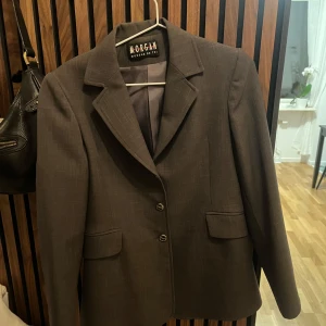 Grå kavaj från Morgan - Snygg grå kavaj från Morgan med klassisk krage och två framfickor. Perfekt för en stilren look. Passar bra till både jeans och mer formella byxor.