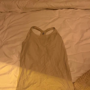 Beige ribbad linnetopp från H&M - Säljer en beige ribbad linnetopp från H&M. Toppen har en sportig design med brottarrygg och är perfekt för en avslappnad stil.