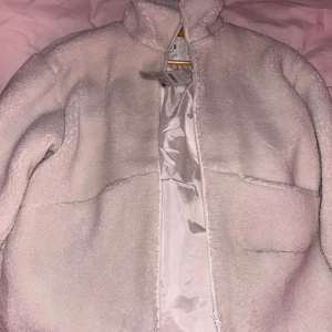 Vit teddyjacka från NAKD - Mysig vit teddyjacka från NA-KD  med dragkedja framtill. Perfekt för kyliga dagar med sin fluffiga och varma design. Jackan har en hög krage och är långärmad, vilket ger extra värme och komfort. Ett måste för garderoben!