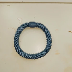 Knekki - Snyggt blått flätat armband med en central pärla. Perfekt för att ge en färgklick till din outfit. Armbandet har en elastisk design som gör det enkelt att ta på och av.