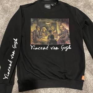 Svart desing tröja - Snygg svart tröja från Koton med ett stort tryck av Vincent van Gogh-målningen 'Potatisätarna' på framsidan. Tröjan har långa ärmar och texten 'Vincent van Gogh' tryckt på ena ärmen. Perfekt för konstälskare!
