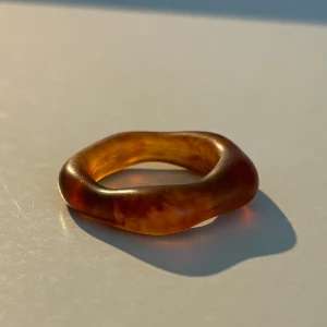 Brun ring i transparent material - Säljer en unik brun ring i ett transparent material med en organisk form. Ringen har en mjuk och rundad design som ger ett naturligt och stilrent intryck. Perfekt för att ge en subtil touch till din stil.