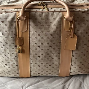 Etro Beige resväska med monogram - Säljer en stor beige resväska från Etro med monogrammönster. Väskan har läderdetaljer och en dragkedja med hänglås för extra säkerhet. Insidan är klädd i en livfull orange färg. Perfekt för resor med stil!