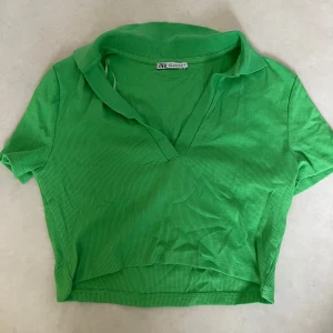 Grön ribbad polotopp från Zara - Snygg grön ribbad polotopp från Zara med korta ärmar och en djup v-ringning. Perfekt för en stilren och bekväm look. Passar bra till både jeans och kjol.