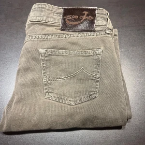 Jacob Cohen - Snygga grå byxor från Jacob Cohen med klassisk design. Byxorna har en normal passform och är tillverkade i ett mjukt material. De har en knappgylf och flera fickor för praktisk användning. Perfekta för en stilren look.