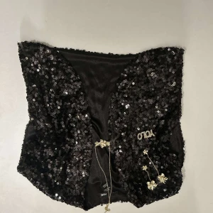 Svart glittrig bolero - Snygg svart bolero från Zara täckt med glittriga paljetter. Perfekt för att lägga till lite glamour till din outfit. boleron har en öppen design och är dekorerad med små blommor i guld.