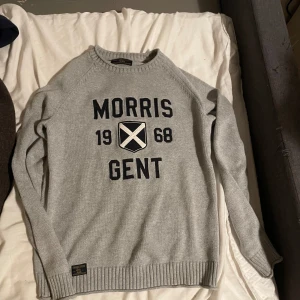 Grå tröja från Morris - Säljer en stilren grå tröja från Morris med texten 'Morris Gent 1968' i svart på framsidan. Tröjan har långa ärmar och ribbstickade muddar vid ärmslut och nederkant. Perfekt för en avslappnad och snygg look.