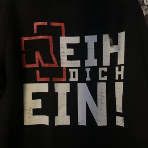 Svart hoodie från Rammstein (official merch) - (Official merch) Säljer en svart hoodie från Rammstein med tryck på bröstet och ärmen. Hoodien har en dragkedja framtill och är långärmad. Perfekt för fans av bandet!