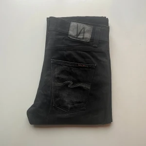 Gritty Jackson Black Rainbow - Svarta jeans från Nudie Jeans. De har en Zipgylf och en subtil logga på bakfickan. 