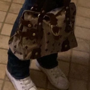 Beige och brun handväska med mönster - Snygg handväska i beige med brunt mönster och detaljer. Väskan har bruna remmar och metallspännen. 