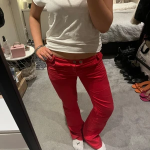 Röda byxor med knappar - Snygga röda byxor med låg midja och bootcut-stil. Byxorna har knappar fram och bakfickor med lock och knapp. Perfekta för en färgglad look.