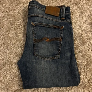 Jeans från nudie jeans  - Snygga mörkblå jeans från Nudie Jeans med klassisk femficksdesign och orange sömmar. Jeansen har en slim passform och är tillverkade i organisk bomull. Perfekta för en avslappnad stil. Har en as najs wash, strlk 32/32. Fraktar antigen samma dag eller dagen därpå, sänker priset 50kr vid snabb och smidig affär💯