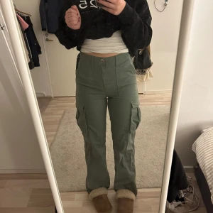 Gröna cargobyxor - Snygga gröna cargobyxor med hög midja och raka ben. Dom kommer ifrån bershka och är andvända fåtal ggr. Dom är i storlek 36/S. Skriv för fler bilder eller bild på!❤️