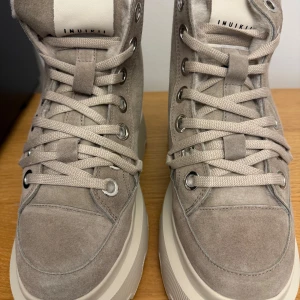 Beige boots från Inuikii - Snygga beige boots från Inuikii i mocka med snörning och en rejäl sula. Insidan är fodrad med mjuk päls för extra värme. Perfekta för kyligare dagar med en stilren design och praktisk dragflik baktill.