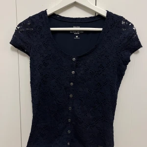 Mörkblå spetsblus från Hollister - Säljer en elegant mörkblå spetsblus från Hollister. Blusen har korta ärmar och knappar framtill. 