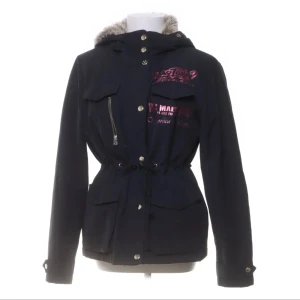 Vinterjacka  - Säljer en svart jacka med pälsfoder och tryck i rosa. Jackan har en huva och stängs med både dragkedja och knappar. Perfekt för kyliga dagar med sin varma insida. Den har också en cool design med text på bröstet och ryggen.