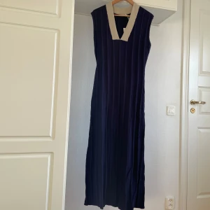 Mörkblå ärmlös klänning M oanvänd  - Snygg mörkblå ärmlös klänning med ribbad struktur och kontrasterande ljus krage. Perfekt för en stilren look. Klänningen har en v-ringad design som ger en elegant touch.
