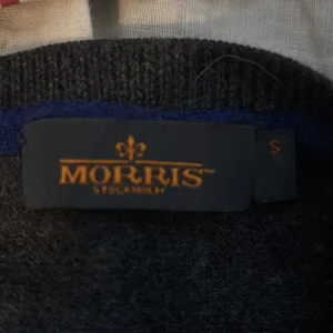 Mörkgrå tröja från Morris - Säljer en stilren mörkgrå tröja från Morris med en diskret broderad detalj på bröstet. Tröjan har en v-ringad hals och långa ärmar,ny pris 1500 mitt pris 350